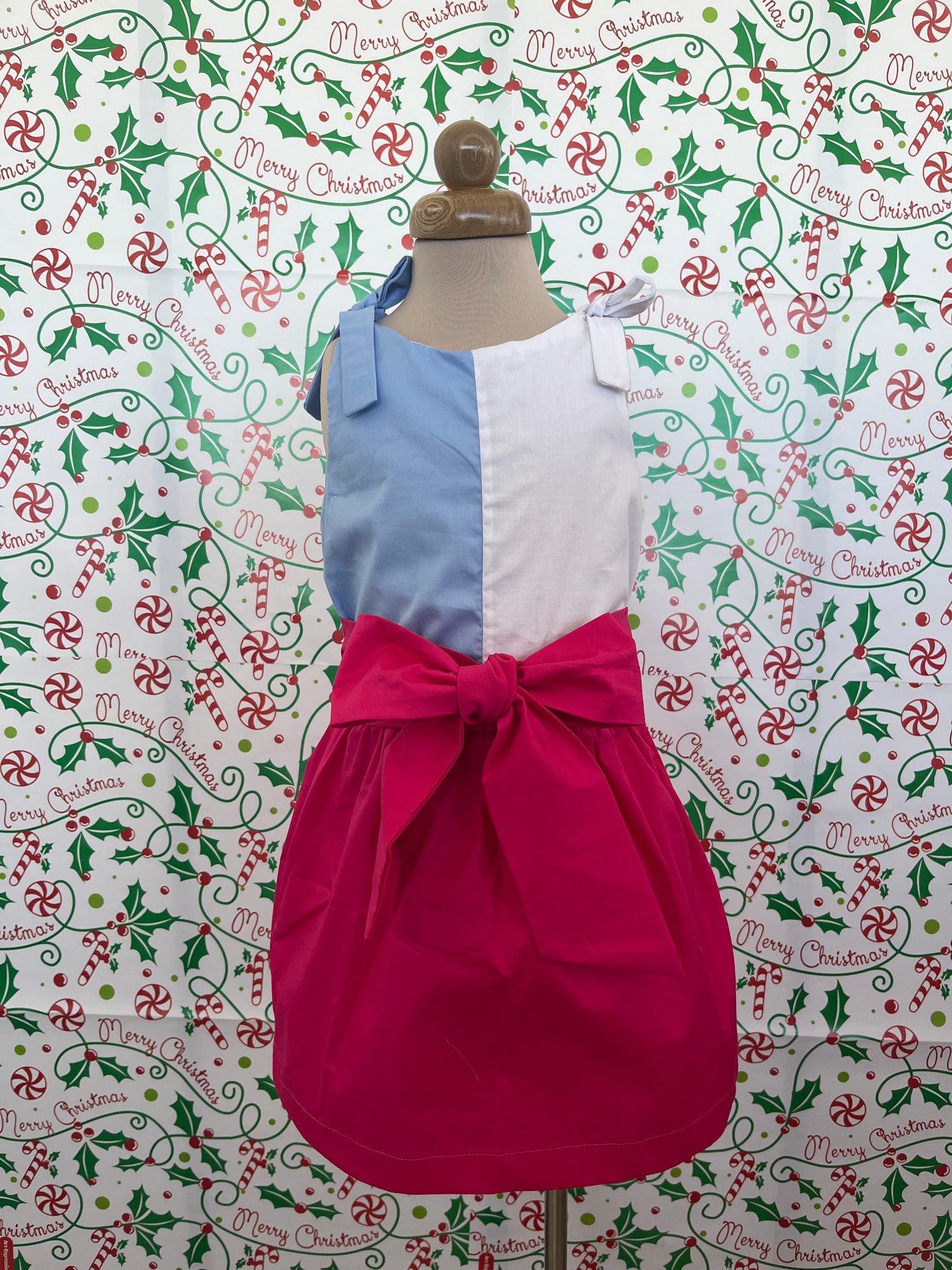 falda fucsia con lazo en la parte frontal, con una blusa blanca y azul claro que se anuda en la parte superior de cada hombro